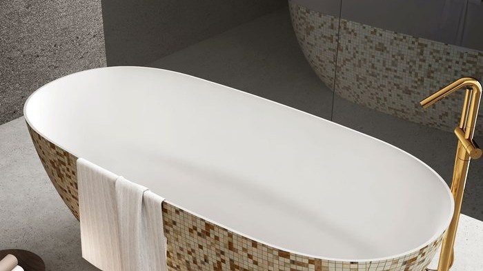 A white freestanding tub with a speckled stone base and a gold floor filler