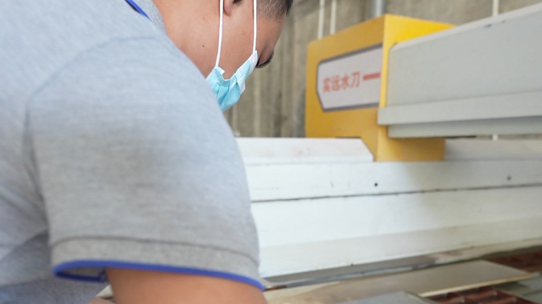 A worker handling a large sheet panel at a cutting machine