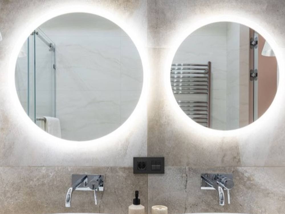 Two round lit mirrors above a pair of countertop basins
