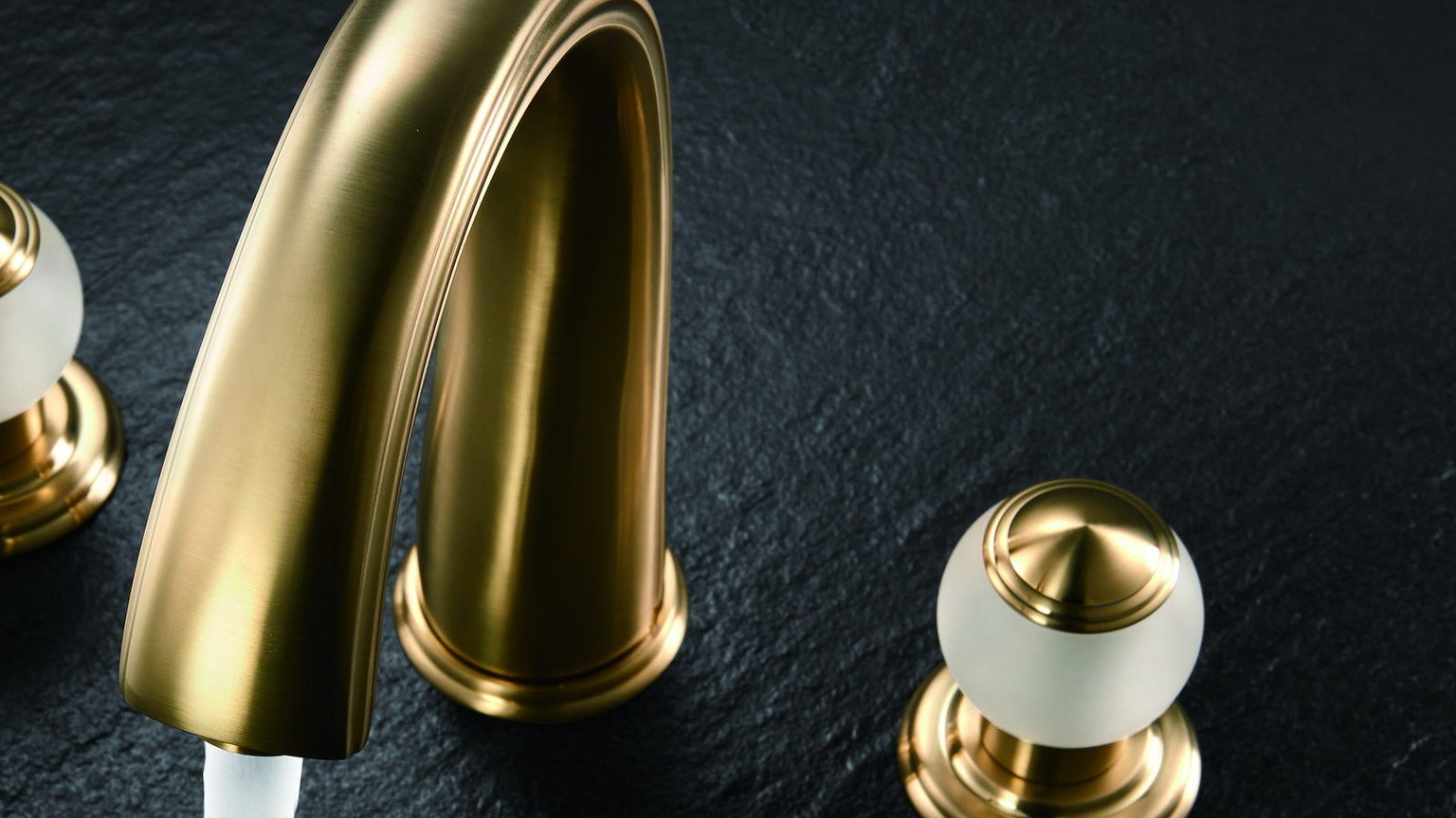 A gold basin faucet running water over dark stone
