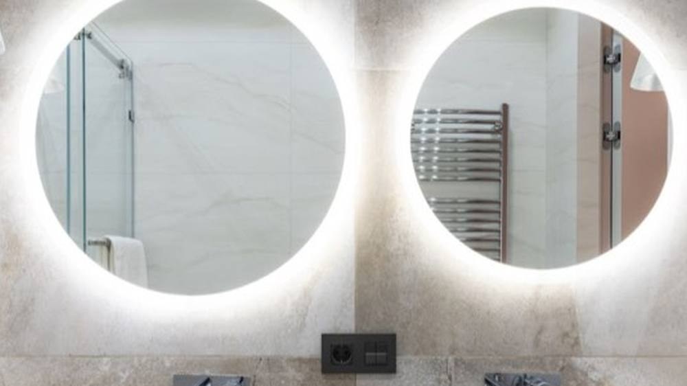 Two round lit mirrors above a pair of countertop basins