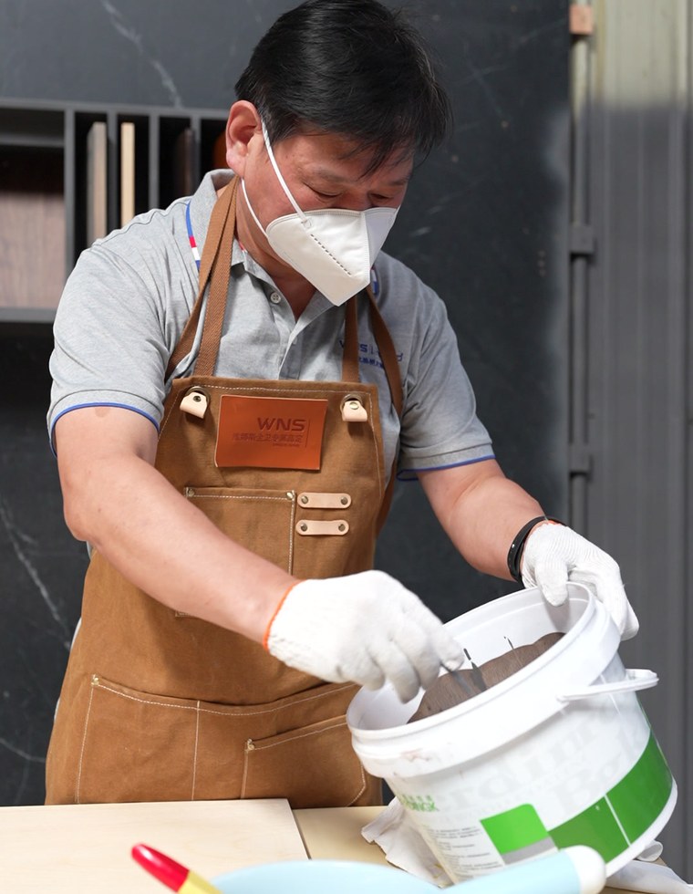 A worker in apron, mask and gloves mixing finish in a bucket