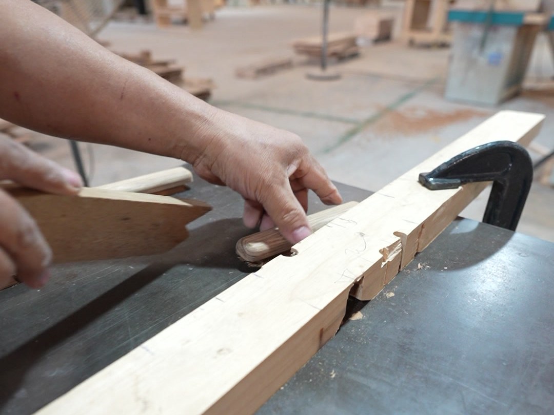 A worker guiding a long timber rail across a machine bed