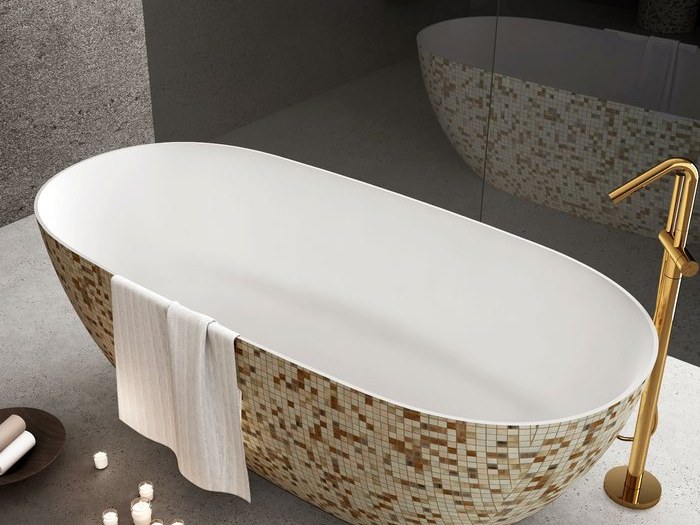 A white freestanding tub with a speckled stone base and a gold floor filler