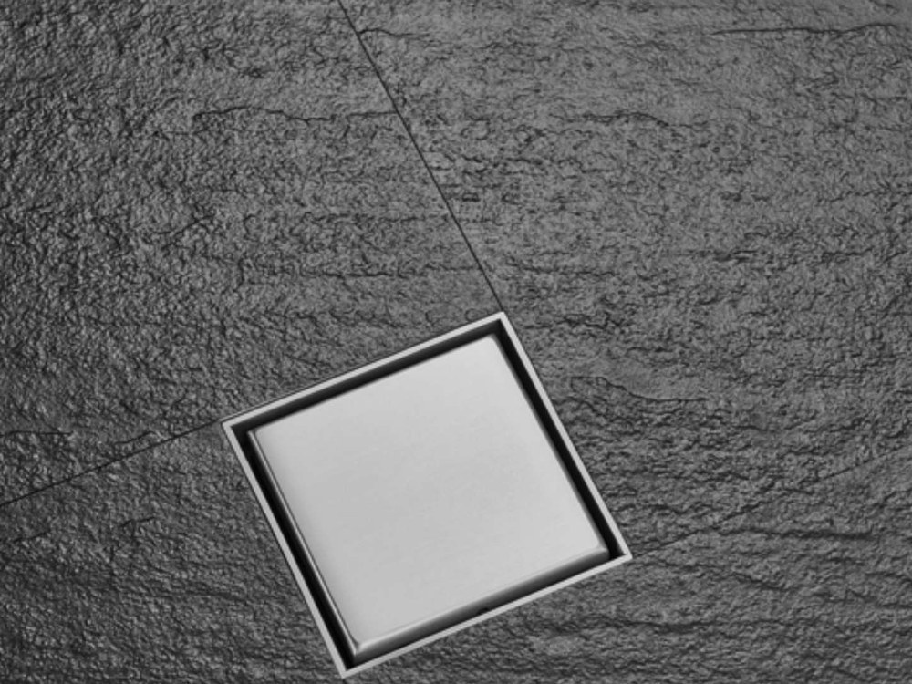 A square stainless floor drain set into dark stone tiling