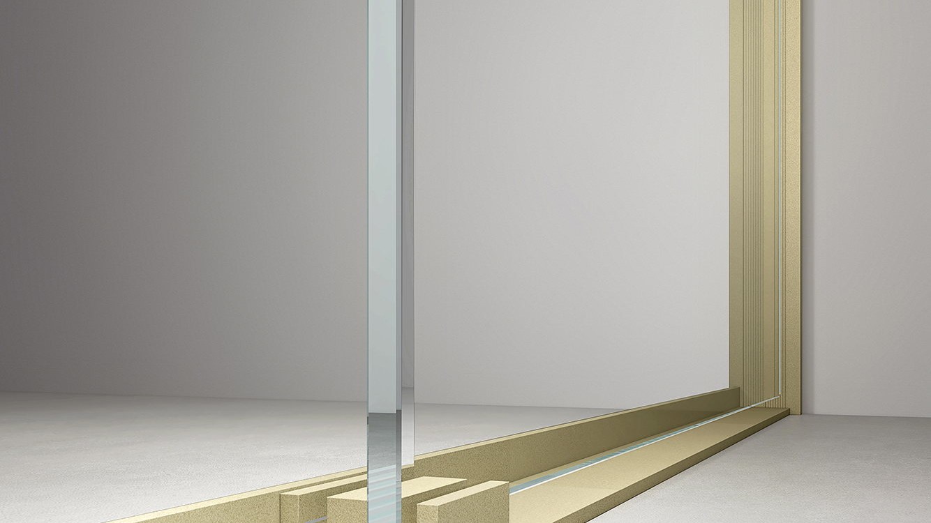 A gold-framed linear drain channel beside a glass screen