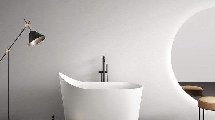 A white freestanding soaking tub beside a floor lamp