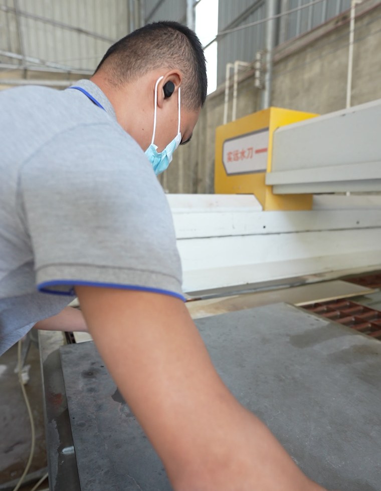 A worker handling a large sheet panel at a cutting machine