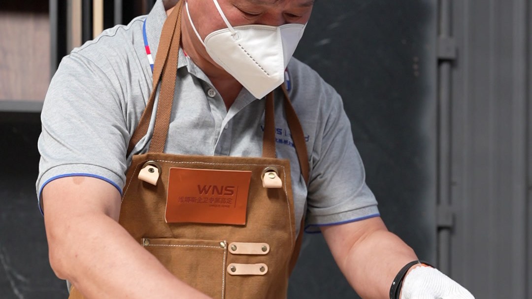 A worker in apron, mask and gloves mixing finish in a bucket