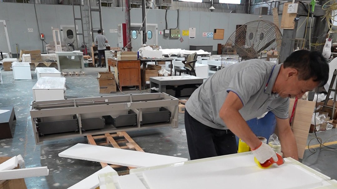 A worker stretch-wrapping a large white panel on a pallet