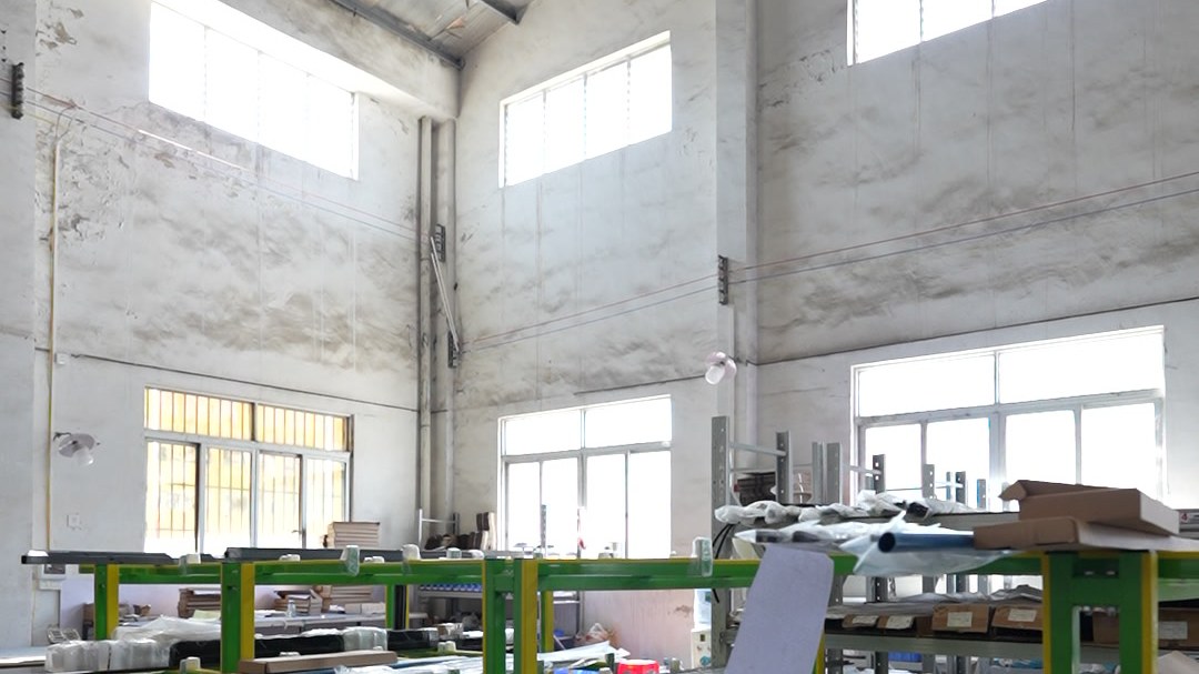 Green and yellow steel assembly racks in a bright shower enclosure production hall