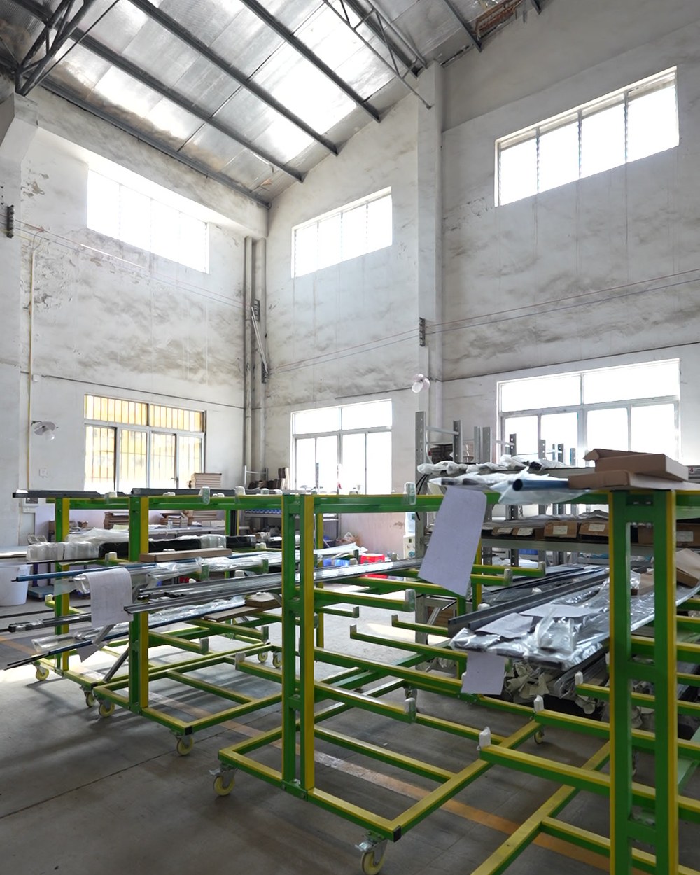 Green and yellow steel assembly racks in a bright shower enclosure production hall