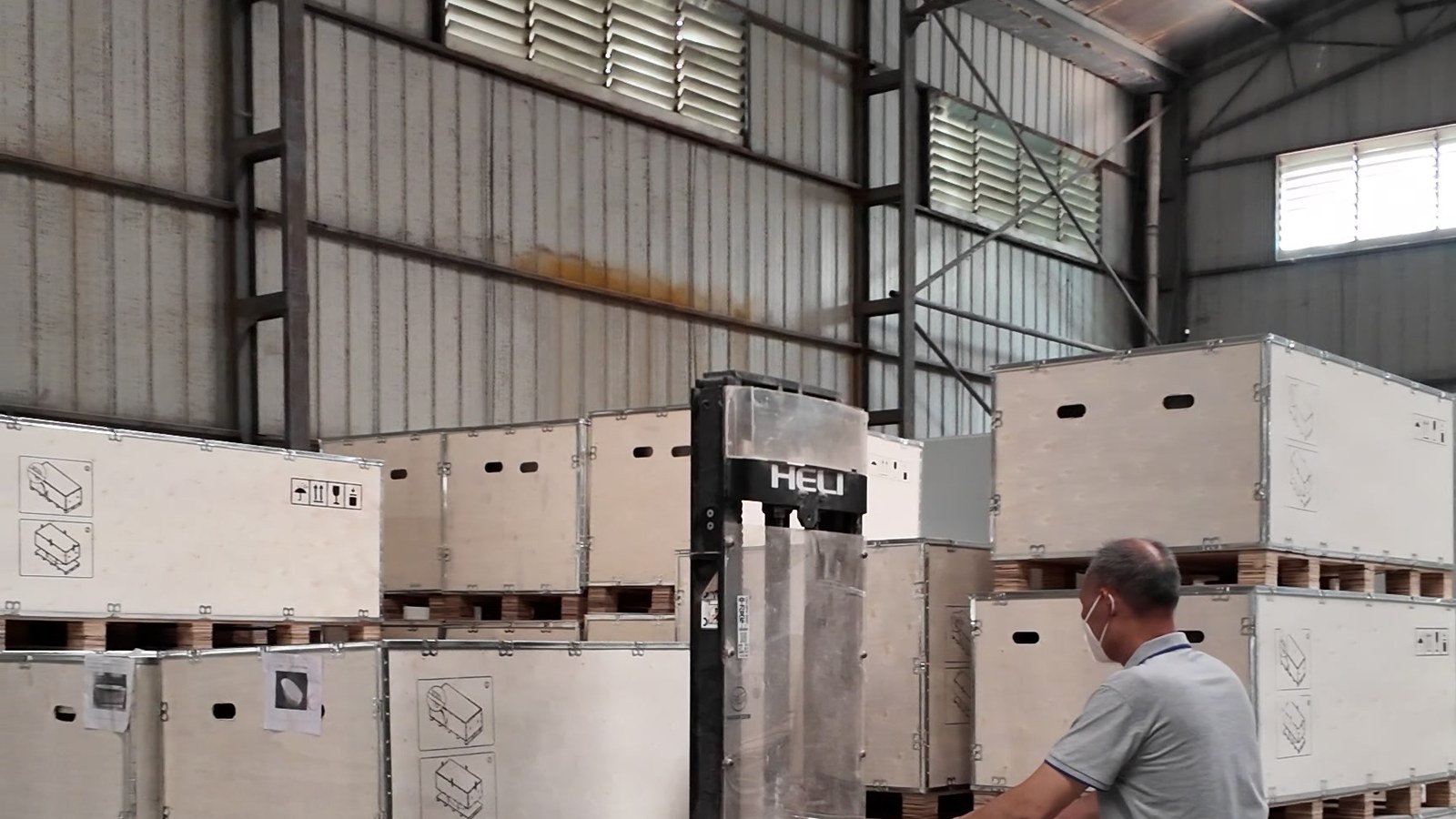 A worker moving crate-packed goods with a pallet truck in the warehouse