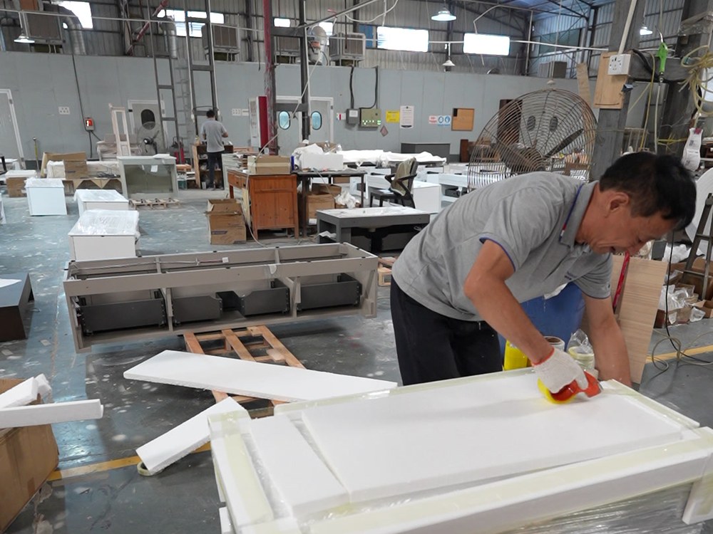 A worker stretch-wrapping a large white panel on a pallet
