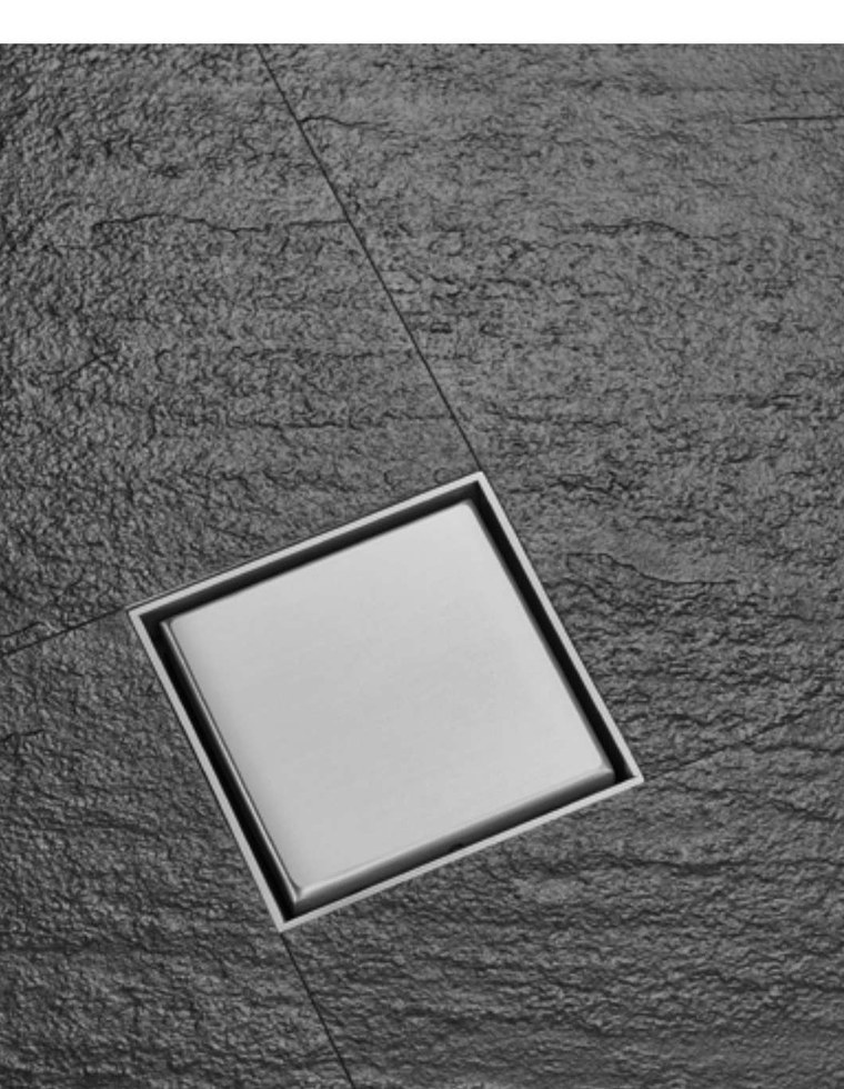 A square stainless floor drain set into dark stone tiling