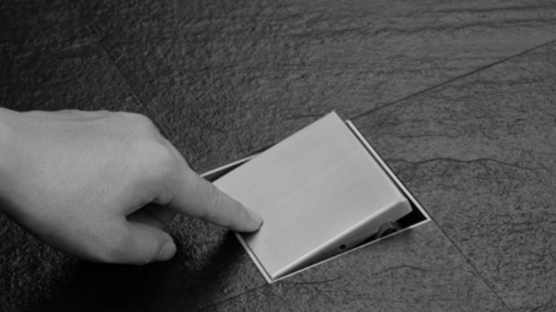A hand lifting the removable cover from a floor drain