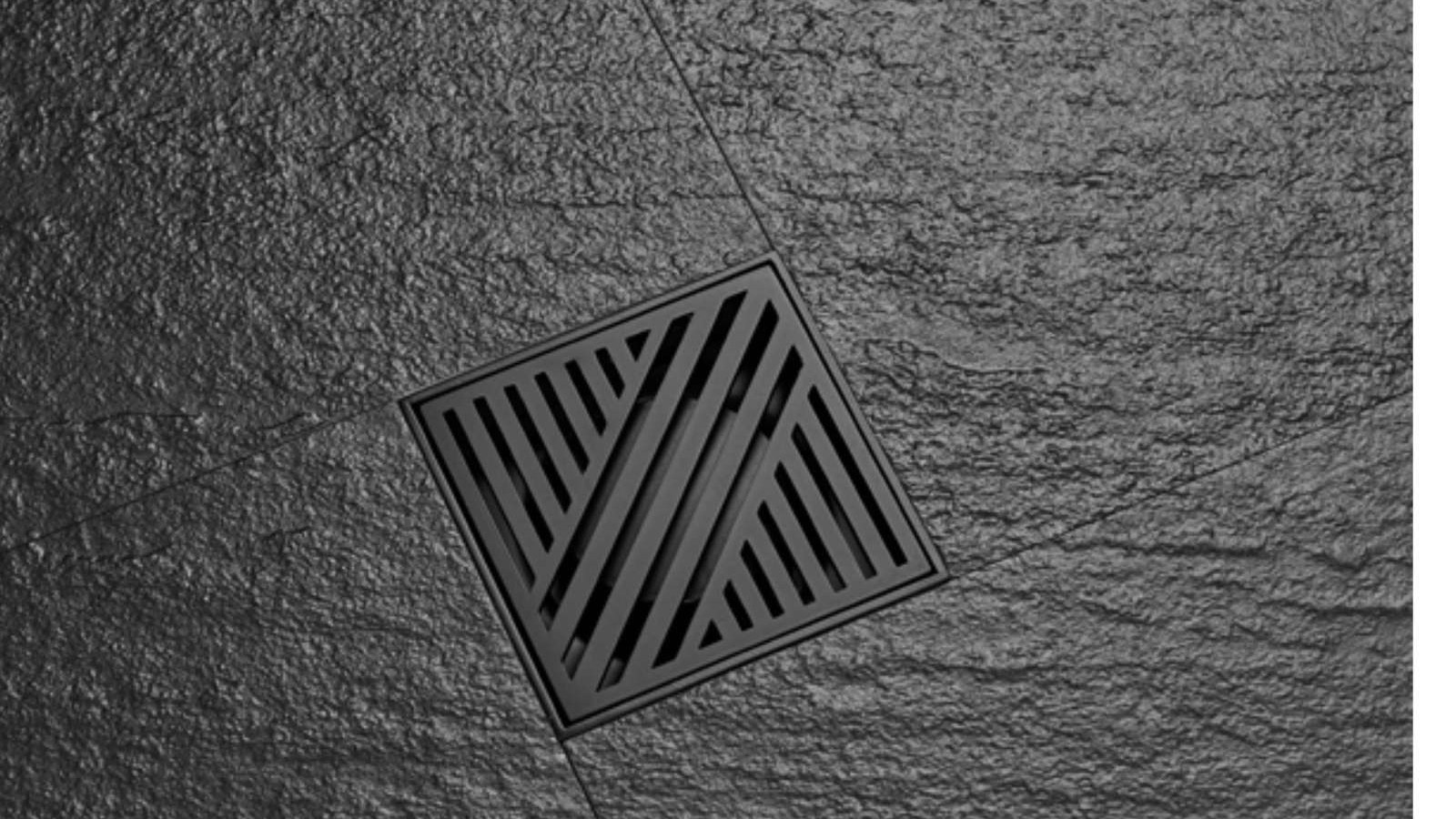 A square floor drain with a slotted grate in dark tiling