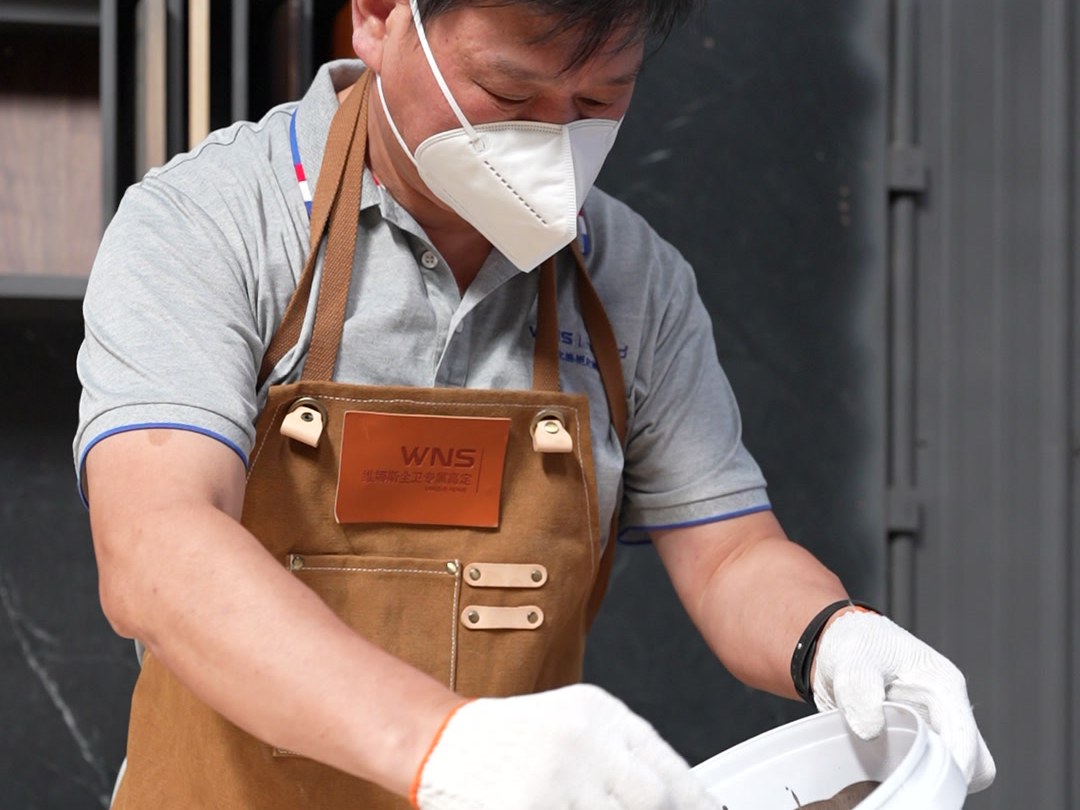 A worker in apron, mask and gloves mixing finish in a bucket