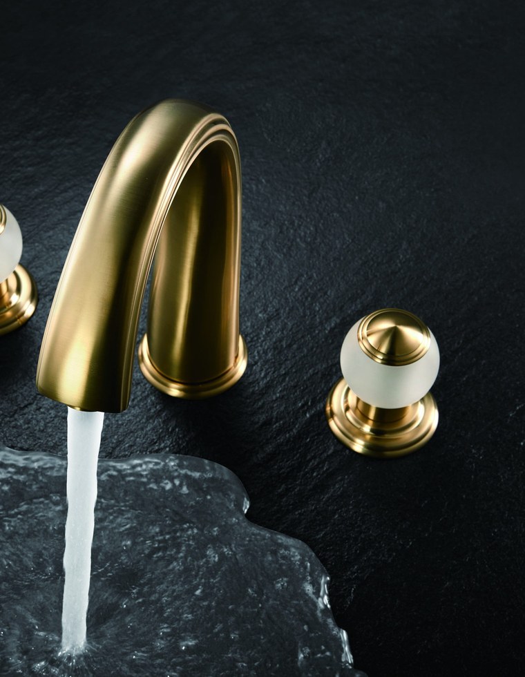 A gold basin faucet running water over dark stone