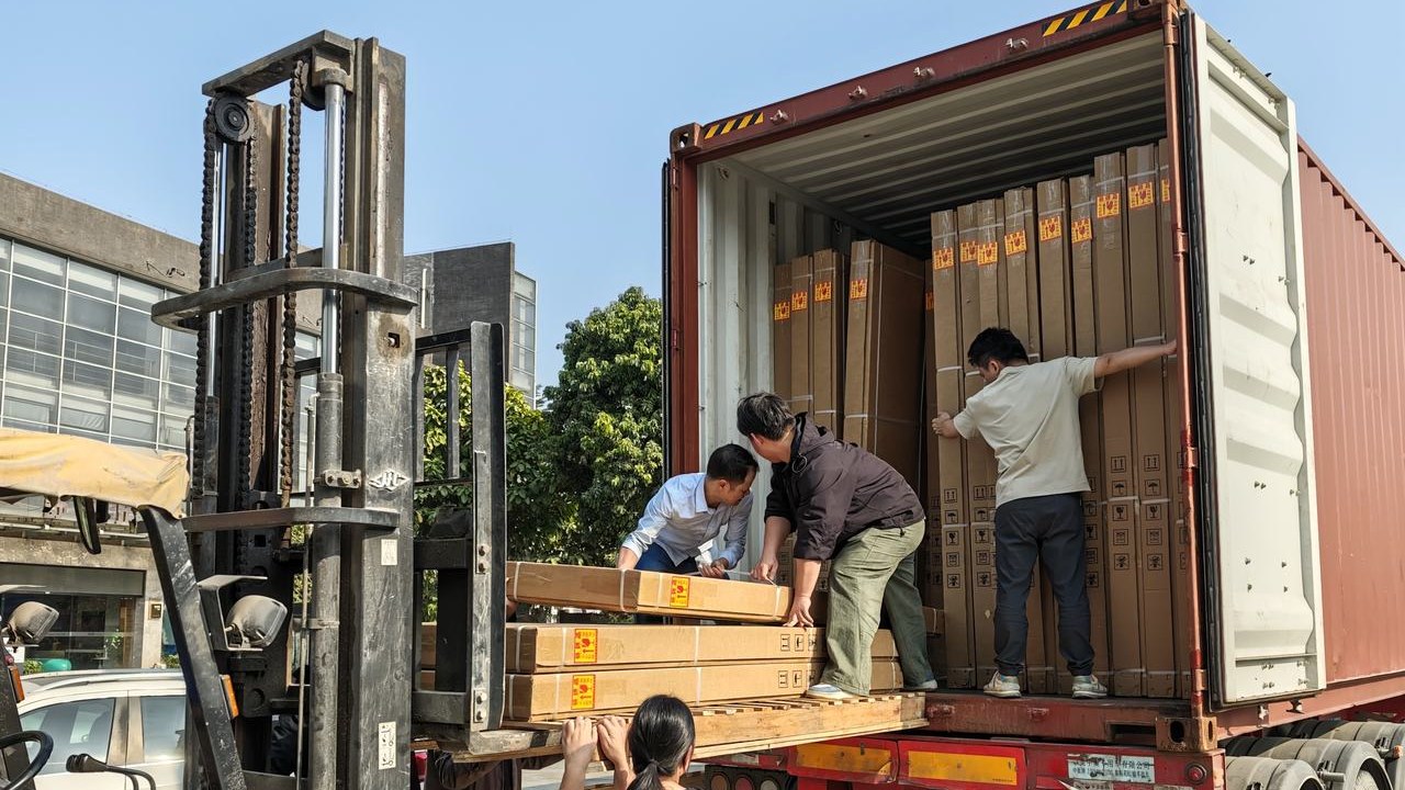 Workers and a forklift loading packed bathroom vanity cartons into a shipping container