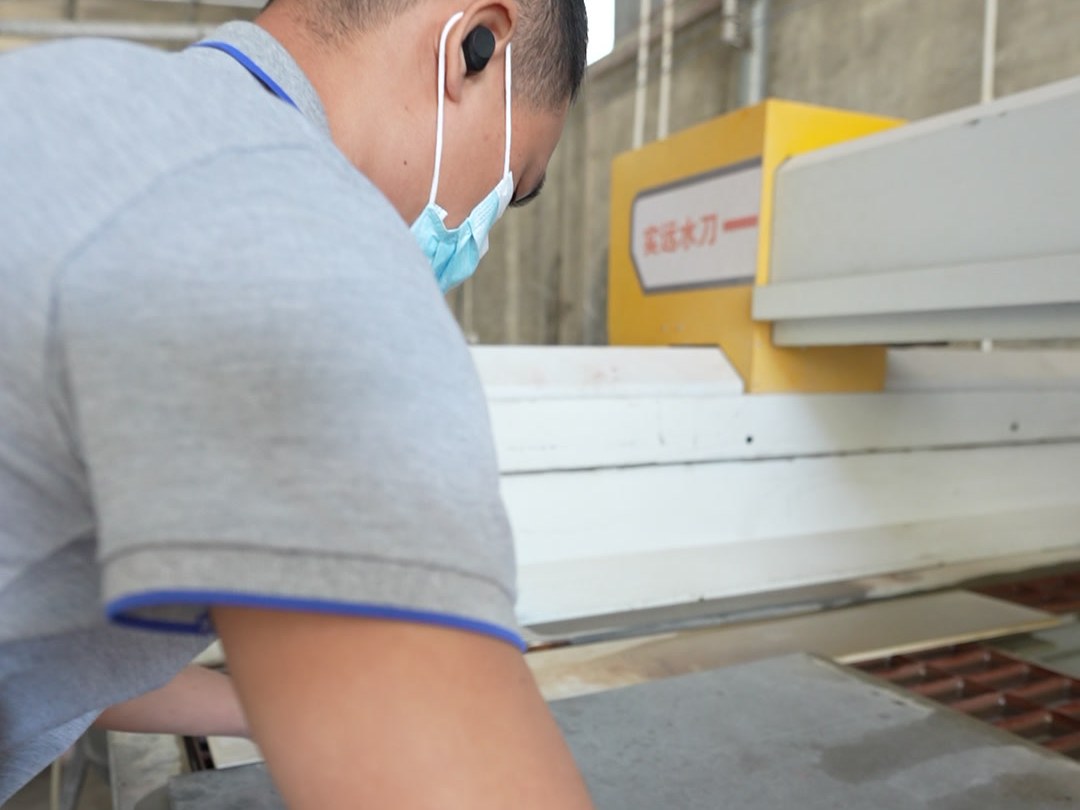 A worker handling a large sheet panel at a cutting machine
