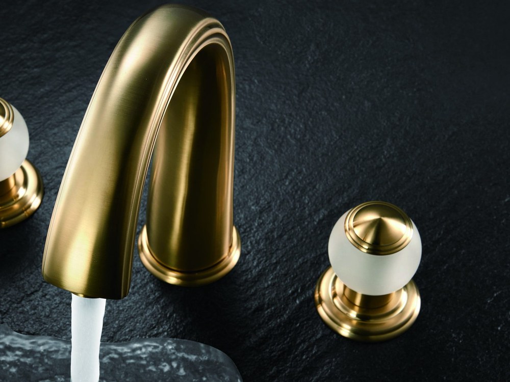 A gold basin faucet running water over dark stone