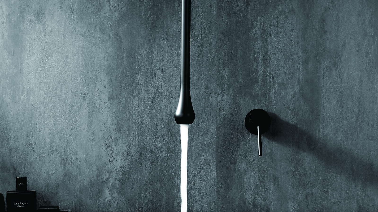 A slim wall-mounted faucet running water into a basin