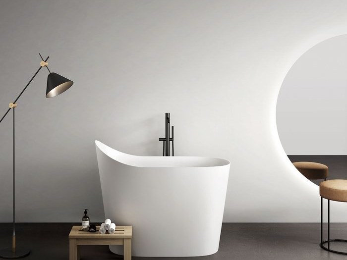 A white freestanding soaking tub beside a floor lamp
