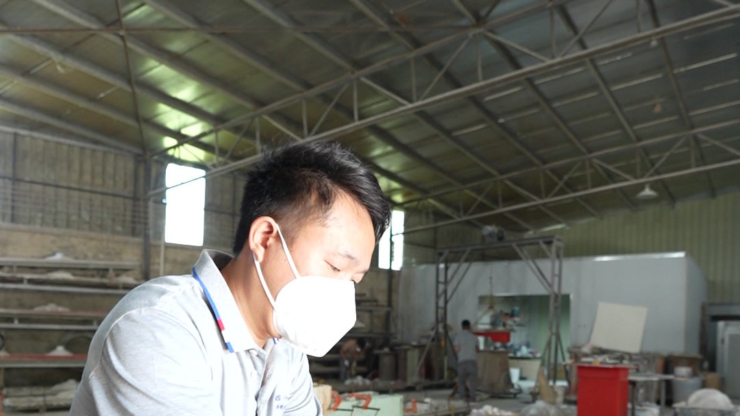 A masked worker leaning into a large round mixing vat in the factory