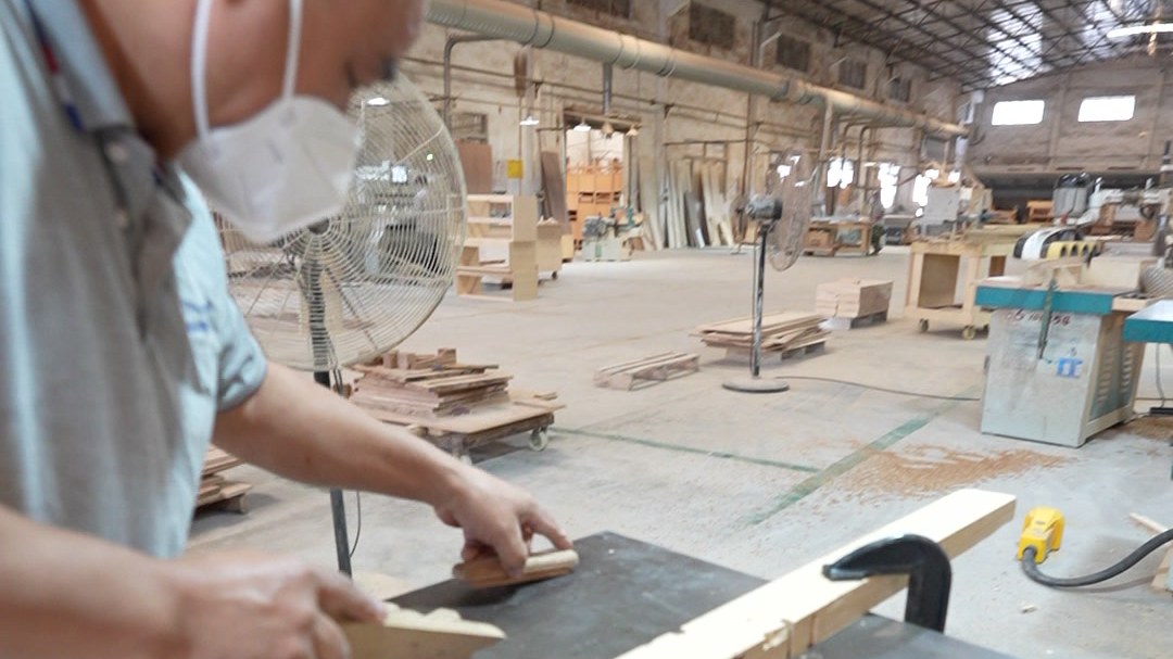 A worker running a long solid wood rail through a bench machine in the workshop