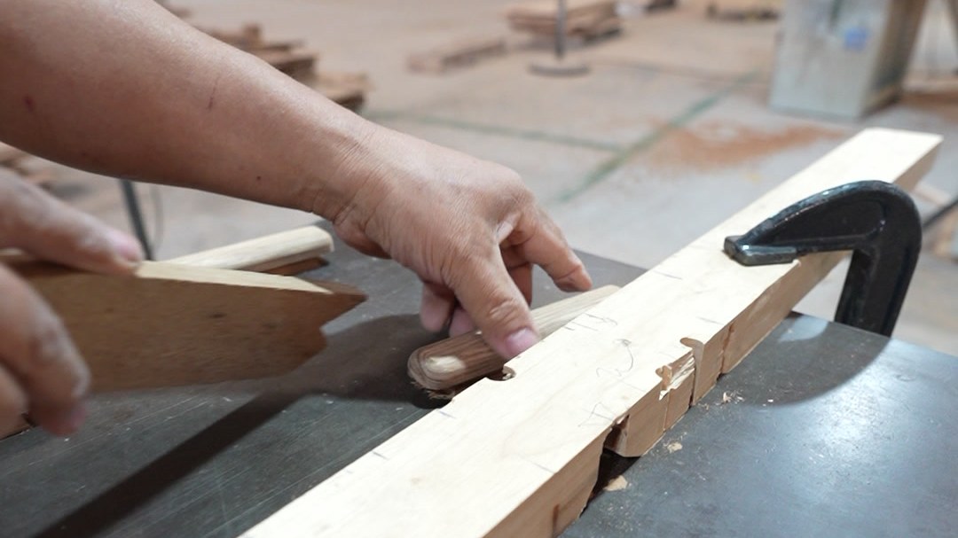 A worker guiding a long timber rail across a machine bed