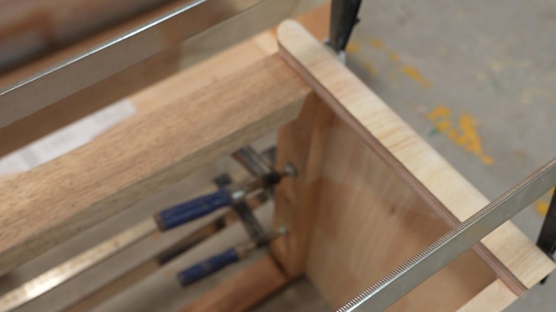 A curved wood panel held in clamps on a press bench