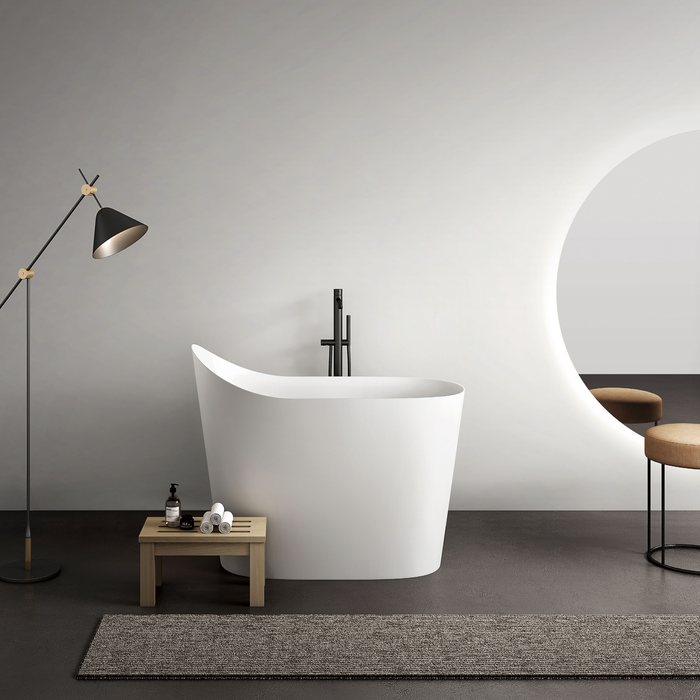 A white freestanding soaking tub beside a floor lamp