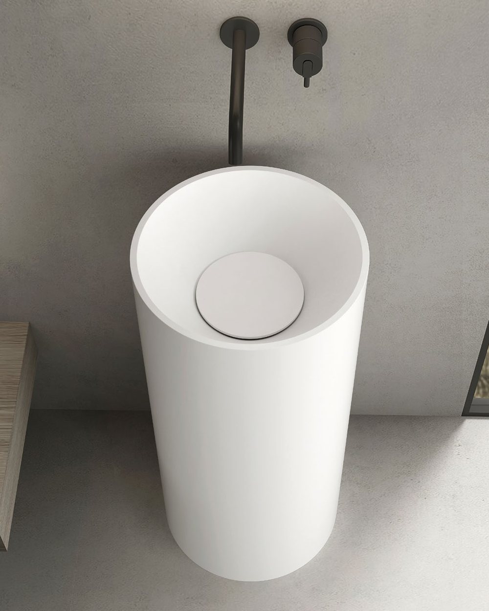 A white solid surface pedestal basin against a plain wall