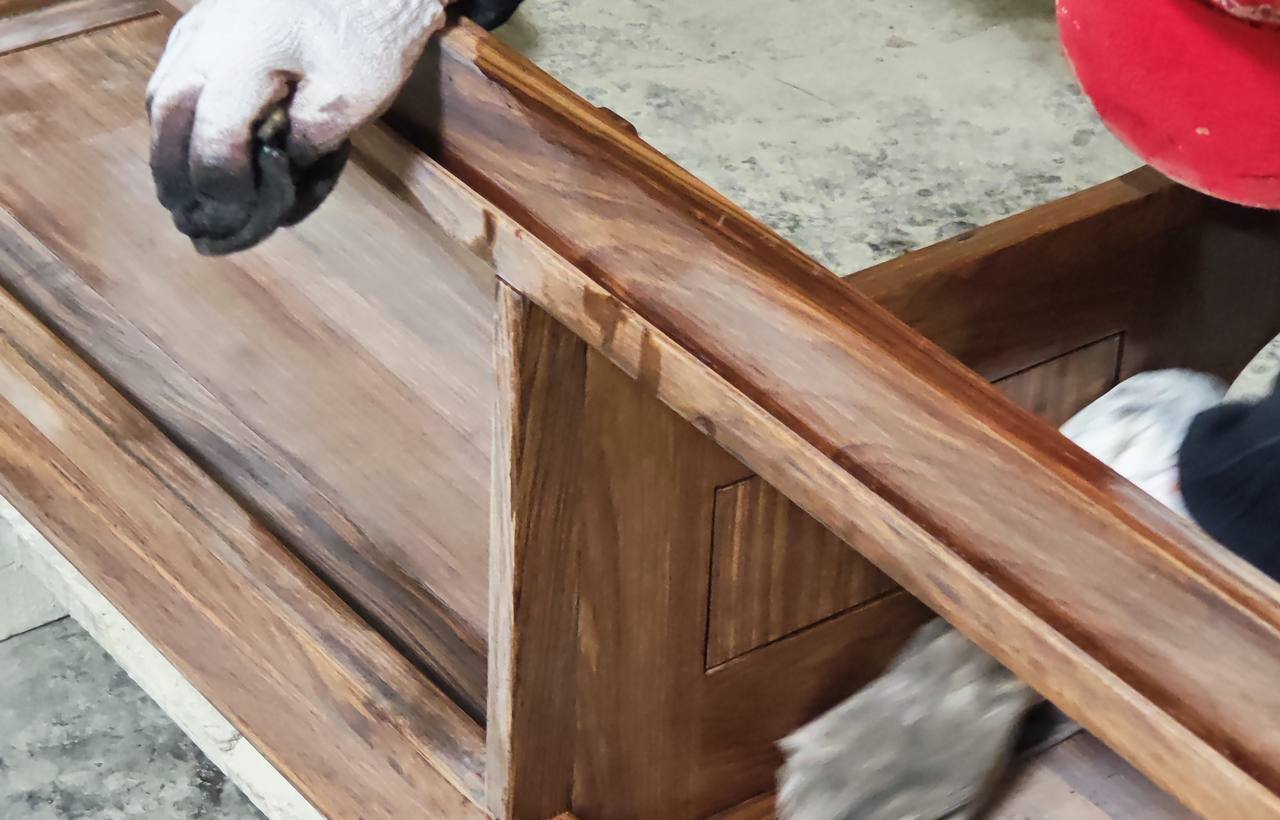 A worker hand-sanding the solid wood frame of a wall-mounted bathroom vanity