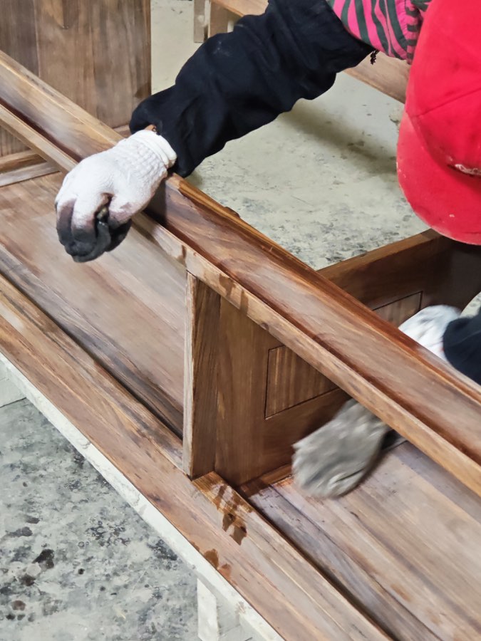 Gloved hands wiping finish onto the solid wood frame of a bathroom vanity